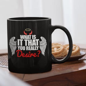 Pode incluir: Caneca de café preta com um design de asa de anjo branca e chifre de diabo vermelho. A caneca tem o texto "What is it that you really desire?" impresso nela.