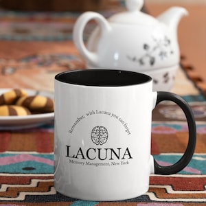 May include: White coffee mug with a black handle and black rim. The mug has a black and white graphic of a brain with the text "Remember, with Lacuna you can forget" and "Lacuna Memory Management, New York".