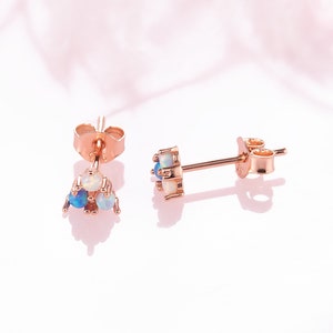May include: A pair of rose gold stud earrings with a cluster of blue and white opals. The earrings have a simple post design.