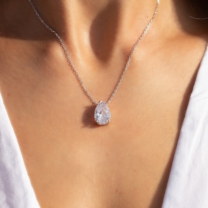 May include: A silver chain necklace with a teardrop-shaped pendant featuring a large, clear cubic zirconia stone.