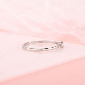 May include: A delicate silver ring with a single small diamond set in the center and smaller diamonds set along the band.