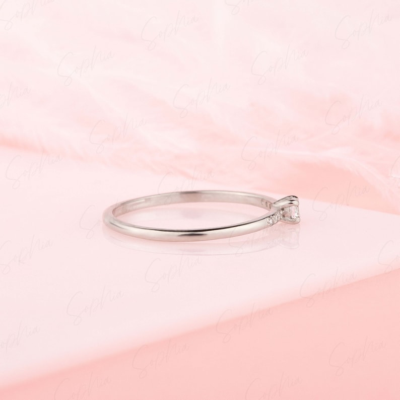 May include: A delicate silver ring with a single small diamond set in the center and smaller diamonds set along the band.