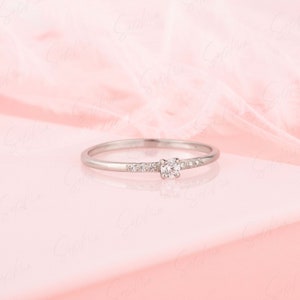 May include: A delicate silver ring with a single round diamond and smaller diamonds set in a band.