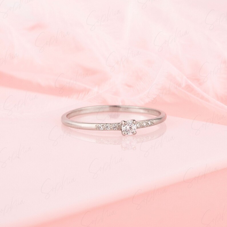 May include: A delicate silver ring with a single round diamond and smaller diamonds set in a band.