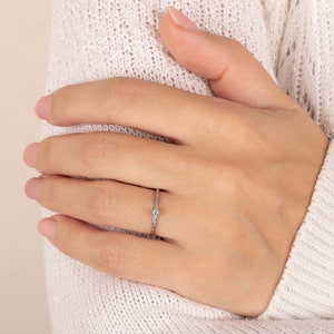 May include: A delicate silver ring with a single round diamond and smaller diamonds set along the band.