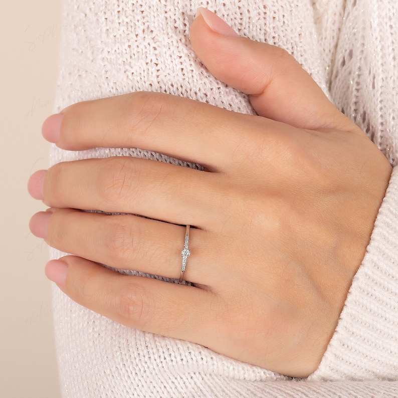 May include: A delicate silver ring with a single round diamond and smaller diamonds set along the band.