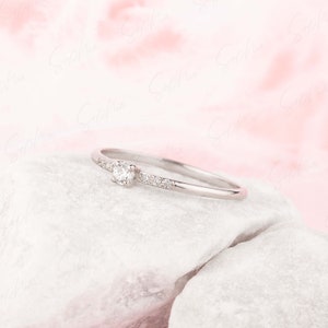 May include: A delicate silver ring with a single round diamond and smaller diamonds set along the band.