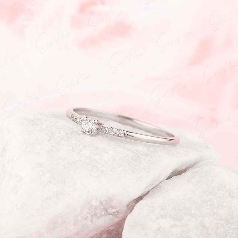May include: A delicate silver ring with a single round diamond and smaller diamonds set along the band.