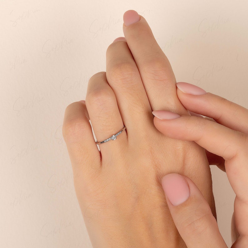 May include: A delicate silver ring with a small, clear gemstone in the center and smaller gemstones on either side.