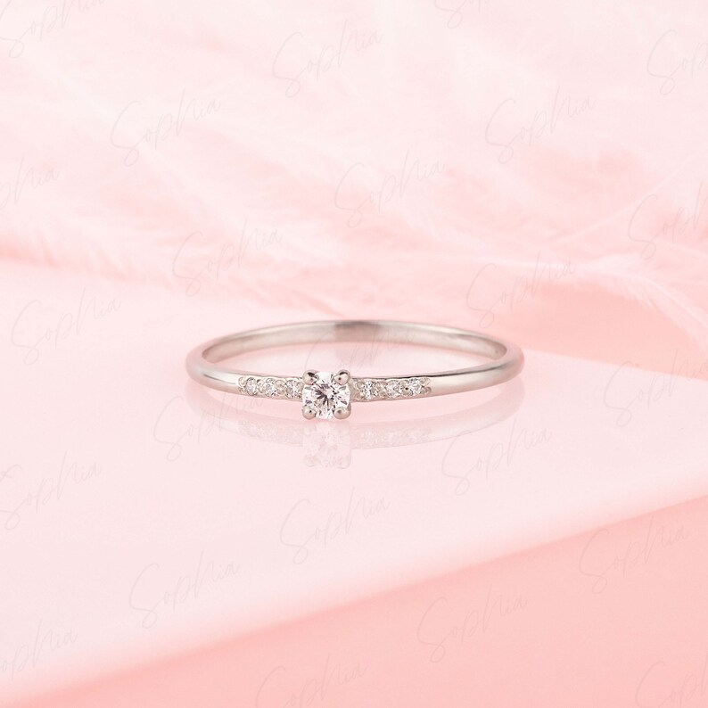 May include: A delicate silver band ring with a single round diamond and smaller diamonds set along the band.