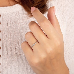 May include: A delicate silver ring with a single round diamond in the center and smaller diamonds on the band.