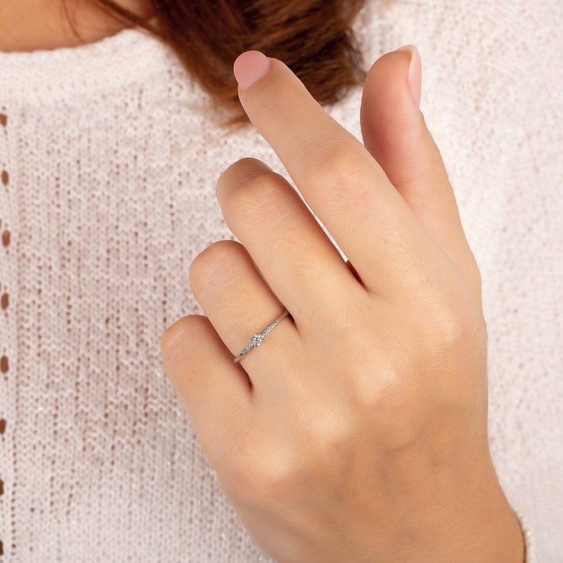May include: A delicate silver ring with a single round diamond in the center and smaller diamonds on the band.