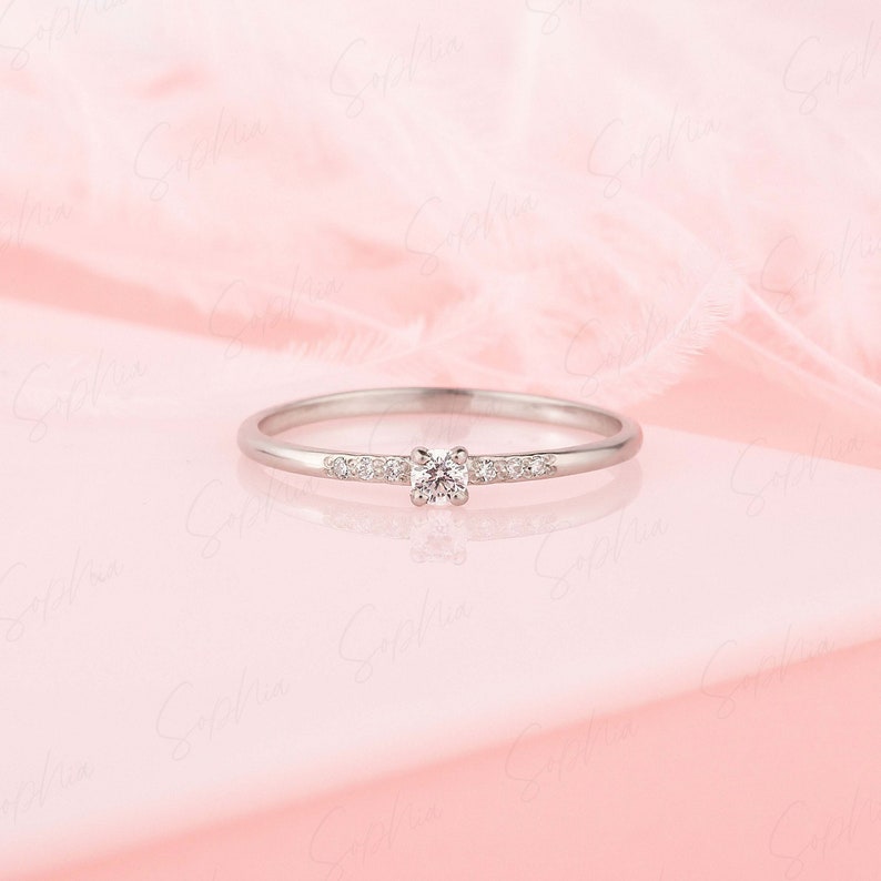 May include: A delicate silver band ring with a small, clear diamond in the center and smaller diamonds set along the band.
