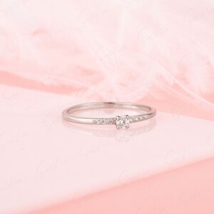 May include: A delicate silver ring with a single round diamond and smaller diamonds set in a band.