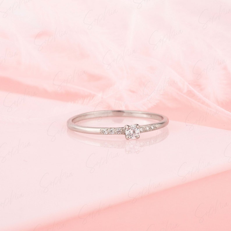 May include: A delicate silver ring with a single round diamond and smaller diamonds set in a band.