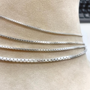May include: Four silver box chain necklaces of varying lengths, displayed on a tan fabric background.