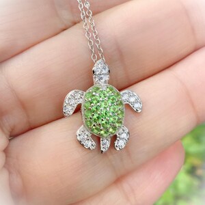 May include: A silver turtle pendant necklace with a green gemstone shell and clear gemstones around the edges.