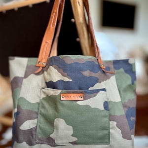 May include: A camouflage tote bag with brown leather straps and a brown leather patch that says "ROSA & CO."