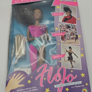 May include: A boxed FloJo fashion doll featuring Florence Griffith Joyner. The doll wears a pink top and blue and pink shorts. The box includes images of fashion and fitness, and the text "LET YOUR DREAMS RUN FREE". Includes nail stickers.