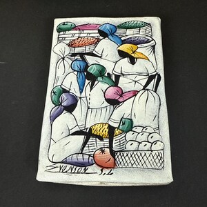 May include: A rectangular, hand-painted relief sculpture depicting a market scene. The artwork features figures in white clothing and colorful headscarves, surrounded by baskets of produce. The artist's signature, "Yenson S.L.", is visible.