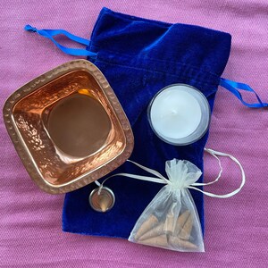 May include: A blue velvet pouch with a white drawstring bag containing incense cones, a small copper bowl, and a white candle.