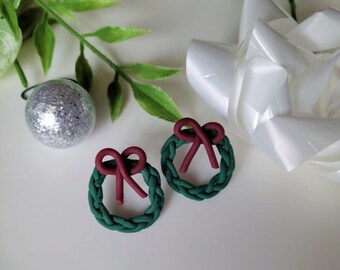 May include: A pair of green and burgundy Christmas wreath earrings. Each earring features a green wreath with a burgundy bow.