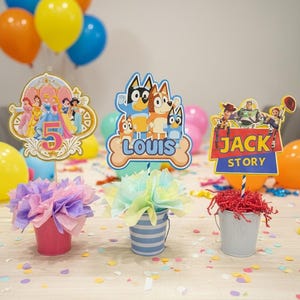 Puede incluir: Decoraciones coloridas para fiestas de cumpleaños con recortes de personajes, globos y cubos decorativos. Los recortes incluyen princesas de Disney, personajes de Bluey y Toy Story. Los cubos contienen flores de papel de seda y papel triturado.