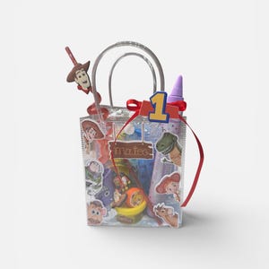K&ouml;nnte beinhalten: Eine transparente Plastik-Geschenkt&uuml;te gef&uuml;llt mit Partyzubeh&ouml;r zum Thema Toy Story. Die Tasche hat ein rotes Band, eine Eins und einen Woody-f&ouml;rmigen Lolli. Aufkleber von Charakteren wie Buzz Lightyear und Rex sind sichtbar.