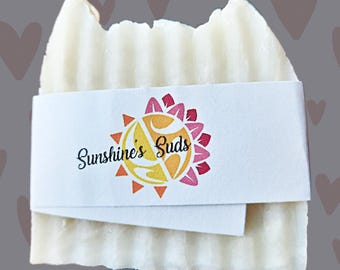 May include: A white bar of soap with a label that says "Sunshine's Suds" and a sun and flower design.