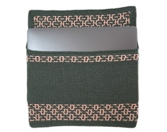 May include: A dark green crocheted laptop sleeve with a pink geometric pattern around the edges. The sleeve is open and a laptop is inside.