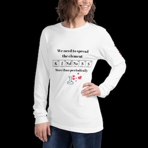 Puede incluir: Camiseta blanca de manga larga con un gráfico negro que dice "We need to spread the element KINDNESS more than periodically". El gráfico presenta una tabla periódica con las letras KINDNESS deletreadas usando los símbolos químicos de los elementos. Hay un pequeño vaso de precipitados con corazones flotando encima.