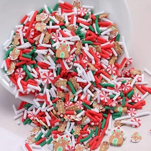 May include: A white bowl overflowing with Christmas-themed polymer clay sprinkles. The sprinkles include red, white, and green rods, gingerbread men, gingerbread houses, and peppermint candies. These are ideal for decorating baked goods.