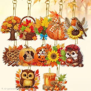 May include: A collection of ten autumn-themed diamond painting ornaments featuring a tree, a basket of leaves, a bouquet, a pumpkin, a bird, a pie, a rabbit, a dog, a hedgehog, an owl, and a candle, each with a gold ball chain.