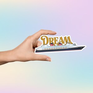 Puede incluir: Una pegatina con un dise&ntilde;o de crucero con la palabra "DREAM" en letras doradas. El barco es blanco con detalles en negro y rojo. La pegatina se sostiene sobre un fondo degradado pastel.