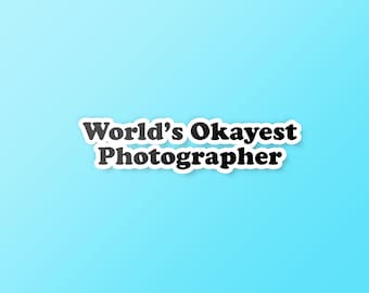 May include: A light blue background with white text that reads "World's Okayest Photographer" in a bold, black font.