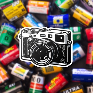 May include: A black and white illustration of a vintage film camera with a large lens. The camera is surrounded by a variety of colorful film canisters.