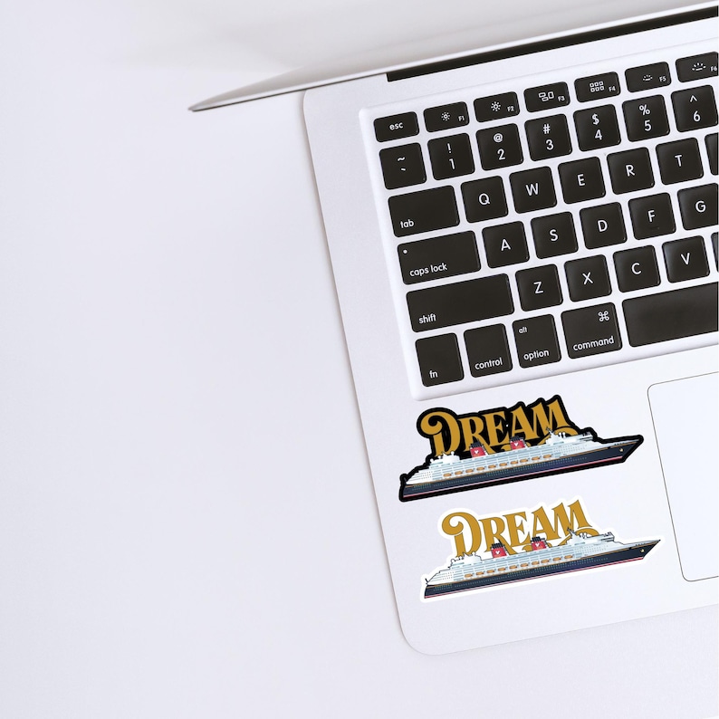 Puede incluir: Dos pegatinas con un dise&ntilde;o de crucero y la palabra "DREAM" en letras doradas. Las pegatinas est&aacute;n colocadas en un port&aacute;til blanco, con el teclado visible. El crucero tiene detalles en rojo y blanco.