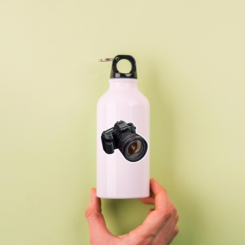 May include: White water bottle with a black camera sticker on the front. The camera is a Canon DSLR with a large lens.