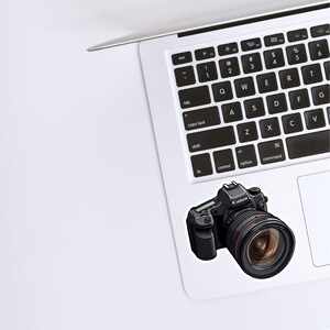 May include: A black Canon DSLR camera with a large lens. The camera has a black body with silver accents and a black lens with a silver ring around the lens.