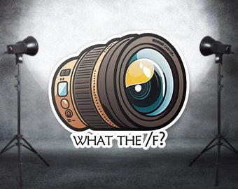 May include: A cartoon illustration of a camera lens with the text "WHAT THE /F?" below it. The lens is surrounded by a white border and is set against a gray background with two studio lights.