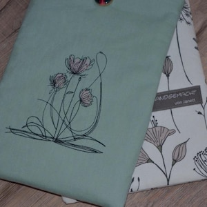 Könnte beinhalten: Eine grüne Stofftasche mit einem floralen Stickmuster. Die Tasche hat ein weißes Stofffutter mit einem Blumenmuster und den Text "Handgemacht von Janett".