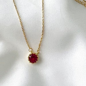 May include: A gold chain necklace with a red gemstone pendant. The pendant is set in a gold crown-shaped setting.