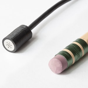 May include: A close-up of a black microphone with a wire and a black and green pencil with a pink eraser.