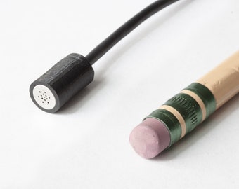 May include: A close-up of a black microphone with a wire and a black and green pencil with a pink eraser.