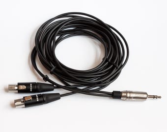 May include: Black audio cable with two REAN XLR connectors and a silver and black 1/4 inch (6.35 mm) connector. The cable is coiled and lies on a white surface. The connectors are black with silver accents.