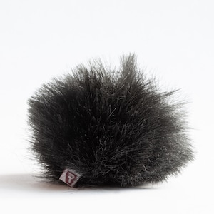Puede incluir: Pantalla de viento de micrófono de color negro y peludo con una pequeña etiqueta marrón con la letra "R".