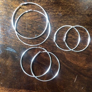 May include: Three pairs of silver hoop earrings of different sizes. The earrings are on a wooden surface.