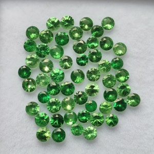 May include: A collection of green gemstones, likely emeralds or peridot, displayed on a white surface. The gemstones are various sizes and shapes, with some having a more rounded form and others being more faceted.