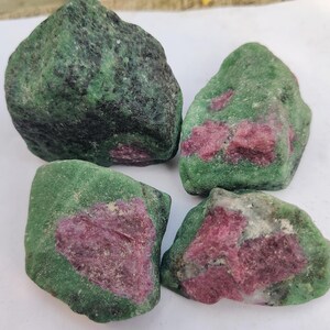 May include: Four rough-cut ruby in zoisite stones. The stones have a dark green exterior with patches of deep red ruby. The stones are irregularly shaped and vary in size, with a natural, unpolished appearance.