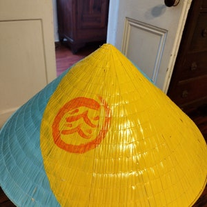 May include: A yellow and blue conical hat with a red and orange symbol on the front. The symbol is a stylized Chinese character.